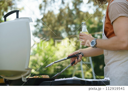 Man grilling on outdoor grill and drinkig lemonade. Outdoor grill or BBQ party in the garden. Man grilling on outdoor grill and drinkig lemonade. Outdoor grill or BBQ party in the garden. 112919541