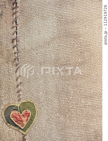 Two pieces of old burlap sewn together with thread and fabric heart. Vertical background with rustic bag texture and Valentine's day decor in patchwork style. Copy space for text Two pieces of old burlap sewn together with thread and fabric heart. Vertical background with rustic bag texture and Valentine's day decor in patchwork style. Copy space for text 112919726