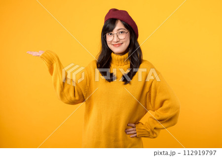 Cute Asian woman 30s with yellow shirt pointing to copy space. Pretty girl model wearing red beret and natural makeup on yellow background. 112919797
