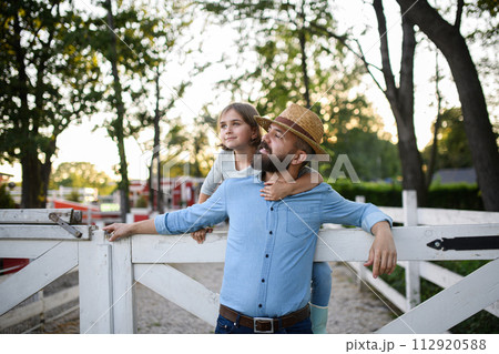 Portrait of farmer family, father and young daughter standing on wooden fence on family farm. Concept of multigenerational farming. 112920588