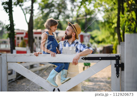 Farmer family, father with daughter sitting on wooden fence on family farm. Concept of multigenerational farming. Farmer family, father with daughter sitting on wooden fence on family farm. Concept of multigenerational farming. 112920673