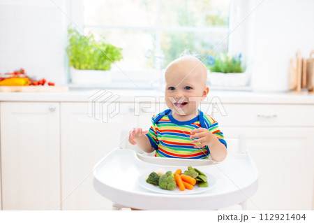Baby eating vegetables in kitchen. Healthy food. Baby eating vegetables in kitchen. Healthy food. 112921404