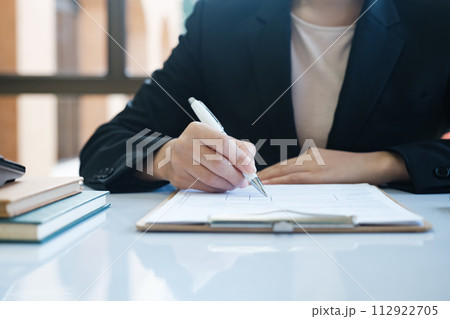 A woman in a suit is writing with a pen on a piece of paper 112922705