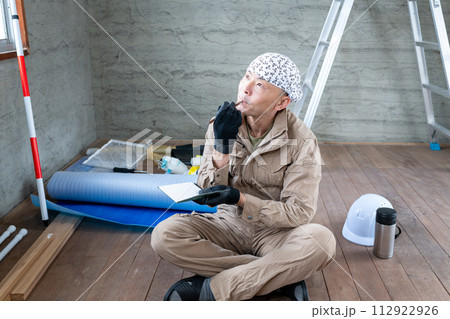 資材倉庫内でメモ帳片手に考え事をする現場系ワーカー 112922926