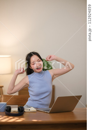 Asian teenage girl studying online on laptop, happy female student celebrating success sitting in living room at home. 112924859