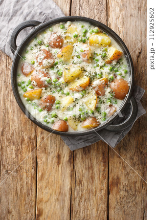 Vegetarian baked potatoes and green peas in creamy cheese sauce close-up in a pan on a wooden table. Vertical top view Vegetarian baked potatoes and green peas in creamy cheese sauce close-up in a pan on a wooden table. Vertical top view 112925602