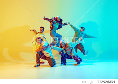 Diverse people, dancers in colorful casual clothes, standing in dynamic jumping pose, performing against gradient green yellow background in neon light. 112926834