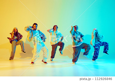 Five dancers, men and women in vibrant casual clothes striking dynamic poses over gradient green yellow background in neon light. 112926846