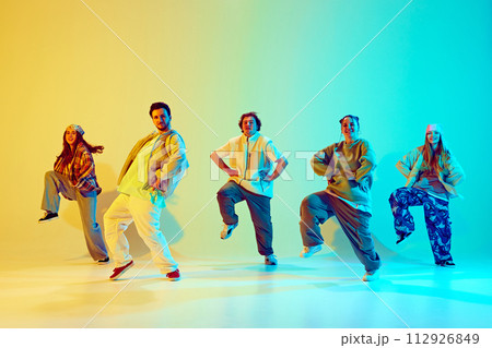 Artistic five dancers, young man and woman in motion, dancing against gradient green yellow background in neon light. Artistic five dancers, young man and woman in motion, dancing against gradient green yellow background in neon light. 112926849