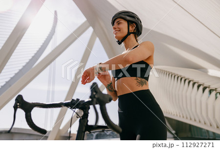Female cyclist in helmet looking at smartwatch and counting calories burned. Healthy life concept  112927271