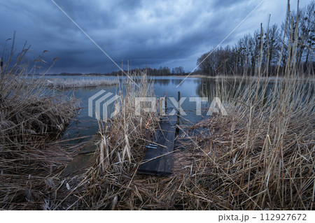 A pier in the reeds and a dark cloud over the lake 112927672