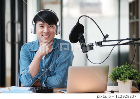 A man wearing headphones is smiling and sitting in front of a laptop 112928237