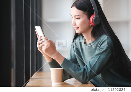 A woman is sitting at a table with a cup of coffee and a cell phone 112928254
