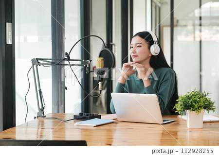A woman is sitting at a desk with a microphone and a laptop 112928255