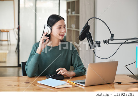 A woman is sitting at a desk with a laptop and a microphone A woman is sitting at a desk with a laptop and a microphone 112928283