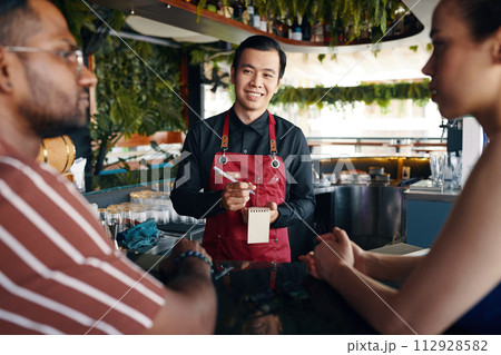 Smiling waiter taking food order in restaurant 112928582