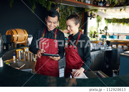 Smiling bartenders checking orders on tablet computer 112928613
