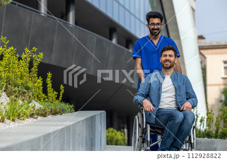 Male nurse in a blue doctors overall carrying a wheelchair 112928822