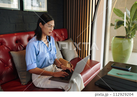 Woman sitting on couch in cafe and working on laptop Woman sitting on couch in cafe and working on laptop 112929204
