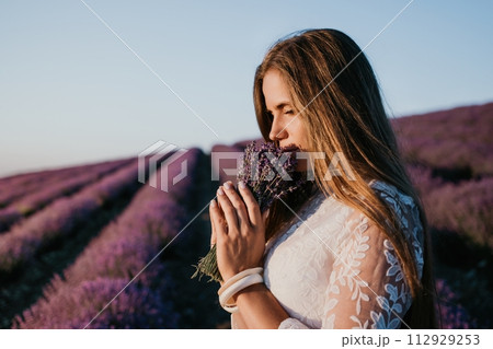 Woman lavender field. Happy carefree woman in a white dress walking in a lavender field and smelling a lavender bouquet on sunset. Ideal for warm and inspirational concepts in wanderlust and travel. Woman lavender field. Happy carefree woman in a white dress walking in a lavender field and smelling a lavender bouquet on sunset. Ideal for warm and inspirational concepts in wanderlust and travel. 112929253