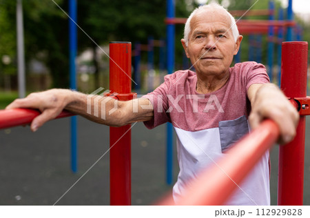 Old man standing between parallel bars outdoors 112929828