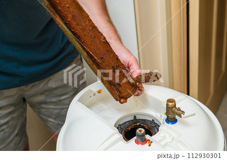 Person holds in his hand a damaged electric heating element from boiler. 112930301