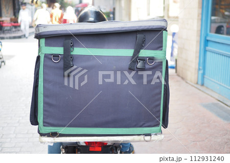Person on scooter with large bag on back, traveling on asphalt 112931240