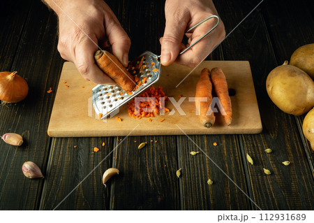 Man cooking in kitchen at home. Cropped image of male hands rubs carrots on a grater. Culinary healthy eating concept 112931689