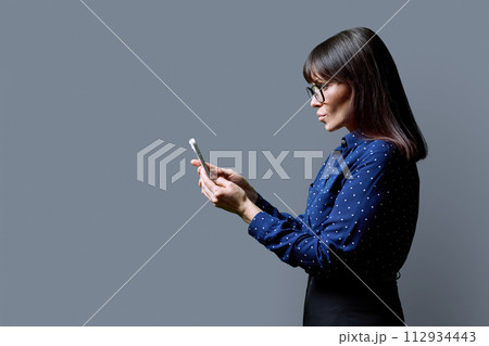 Profile view middle aged woman using smartphone on grey background 112934443