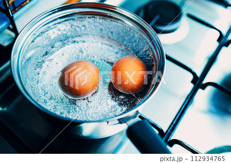 Saucepan stainless steel with two boiling eggs breakfast in a water on a gas stove top view. Saucepan stainless steel with two boiling eggs breakfast in a water on a gas stove top view. 112934765