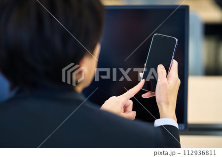 オフィスでデスクワーク中にスマホを操作するスーツの若いビジネスマン 112936811