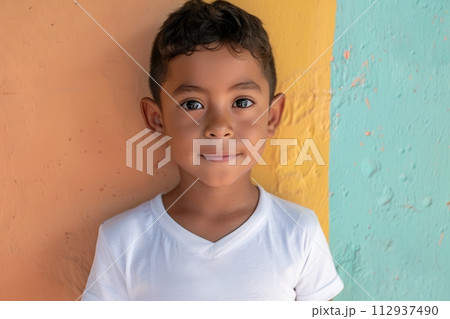 Hispanic child boy 4-6 years old in a white T-shirt without a pattern against the background of a colored wall 112937490