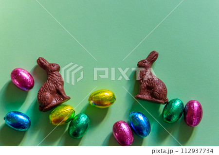 Easter chocolate eggs in foil and Easter chocolate bunnies on green background. Top view 112937734