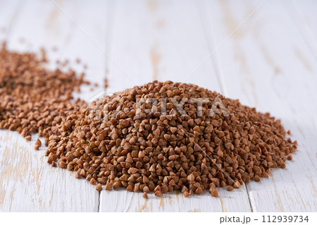 Pile of raw buckwheat on a white wooden table. Heap of organic buckwheat on a white wooden table. Pile of raw buckwheat on a white wooden table. Heap of organic buckwheat on a white wooden table. 112939734