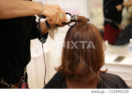 女性の髪にヘアアイロンをかける男性美容師 女性の髪にヘアアイロンをかける男性美容師 112945220
