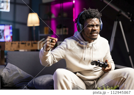 African american player shouting after failing to win videogame, doing frustration gestures. Upset gamer on couch in apartment ready to throw gamepad controller, raging after game over 112945867