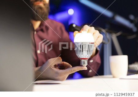 Close up shot of smart light bulb reviewed by tech enthusiast in studio discussing with audience about home improvement, telling viewers latest news in WiFi home automation industry 112945937