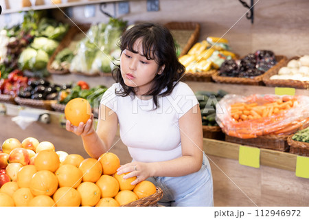 Happy smiling teenage girl making purchases in supermarket, choosing fresh oranges 112946972