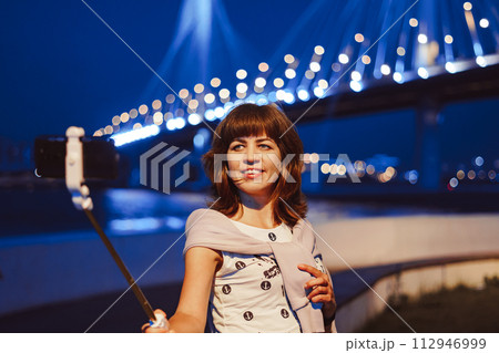 A girl takes pictures of herself on her phone at night in the city 112946999
