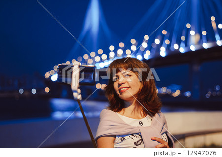 A girl takes pictures of herself on her phone at night in the city A girl takes pictures of herself on her phone at night in the city 112947076