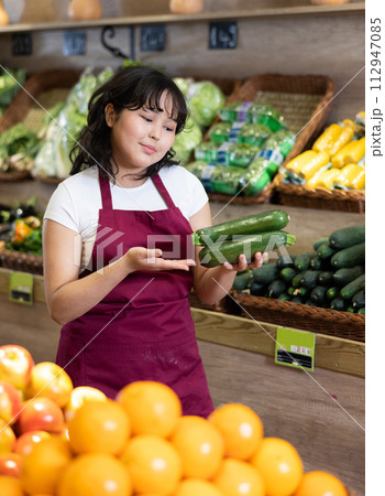 Positive girl seller of grocery supermarket with ripe cucumber in her hands Positive girl seller of grocery supermarket with ripe cucumber in her hands 112947085