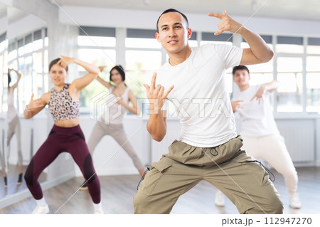 Positive young men and girls dancing modern street dance together during their group training at dance hall 112947270