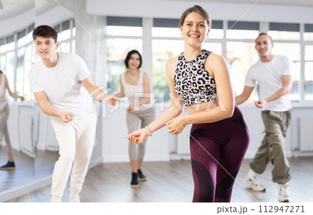 Happy girl and group of young active sport people practicing vogue dancing movements while training twist or charleston in dance hall 112947271