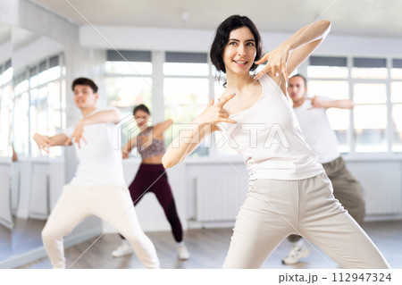Girl enjoys active dancing, learns new movements, moves synchronously with participants of lesson Girl enjoys active dancing, learns new movements, moves synchronously with participants of lesson 112947324