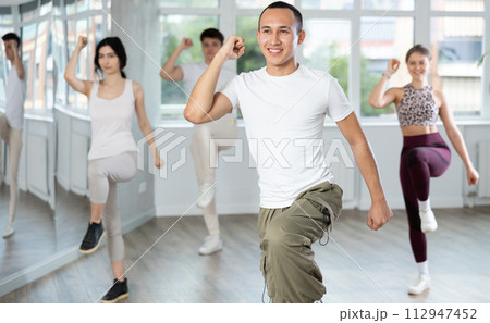 Positive woman and man engaged in dancing in group practices energetic swing in dance studio 112947452