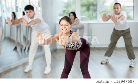 Positive young woman dancing modern dance with other people during group training Positive young woman dancing modern dance with other people during group training 112947687