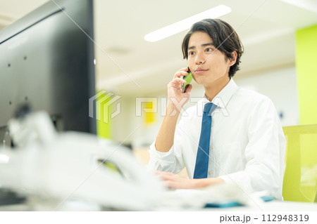 オフィスで電話する若いビジネスマン オフィスで電話する若いビジネスマン 112948319