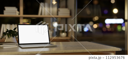 A white-screen laptop computer mockup on a desk in a modern home office at night. 112953676