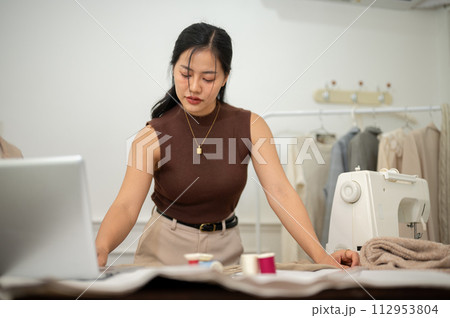 A professional Asian female fashion designer or tailor is focusing on her work in the atelier studio 112953804