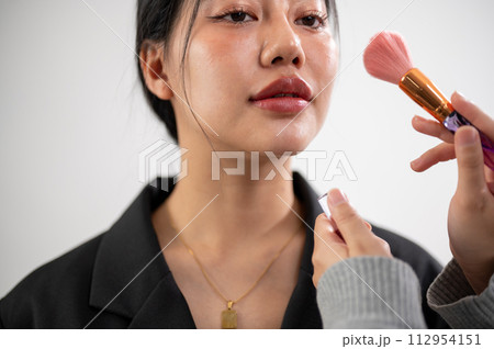 A female model is having makeup applied by a makeup artist, preparing for a photoshoot in the studio 112954151